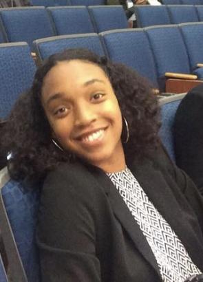 Aara’L Yarber, UCAR fellow, is wearing a black suit jacket and smiles at the camera while sitting in an auditorium. 