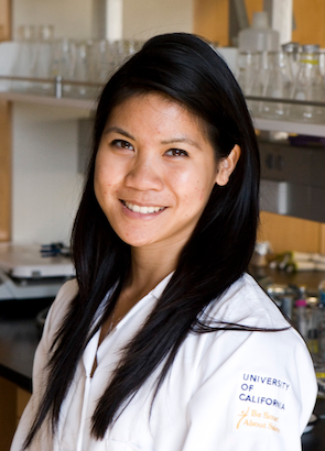 Linh Anh Cát is in a laboratory, wearing a white lab coat and smiling at the camera